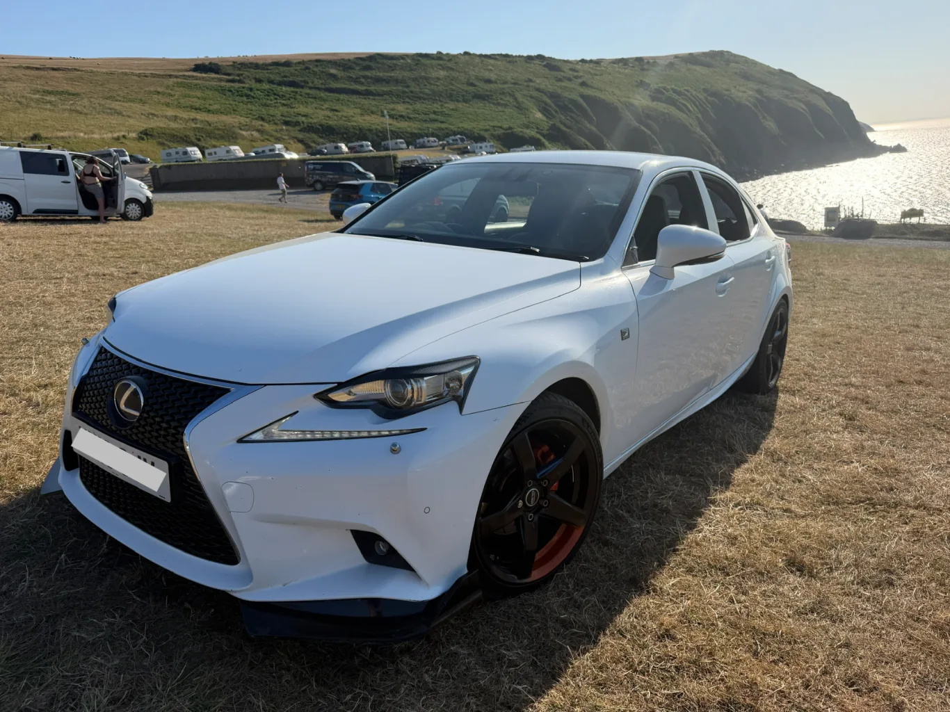 Our former white Lexus IS 300h F Sport photographed by the coast, with black wheels and red accents; registration obscured